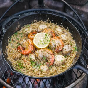 Seafood scampi with pasta, shrimp, herbs, scallops, and lemon in a cast iron skillet over a Breeo fire pit
