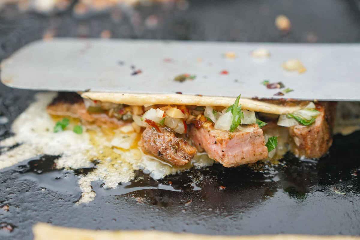 Using a spatula to sear a Spanish garlic oil taco on the griddle 