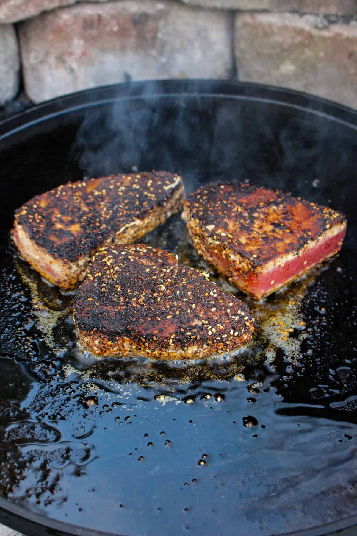 Tuna sizzling in a cast iron pan on the grill.