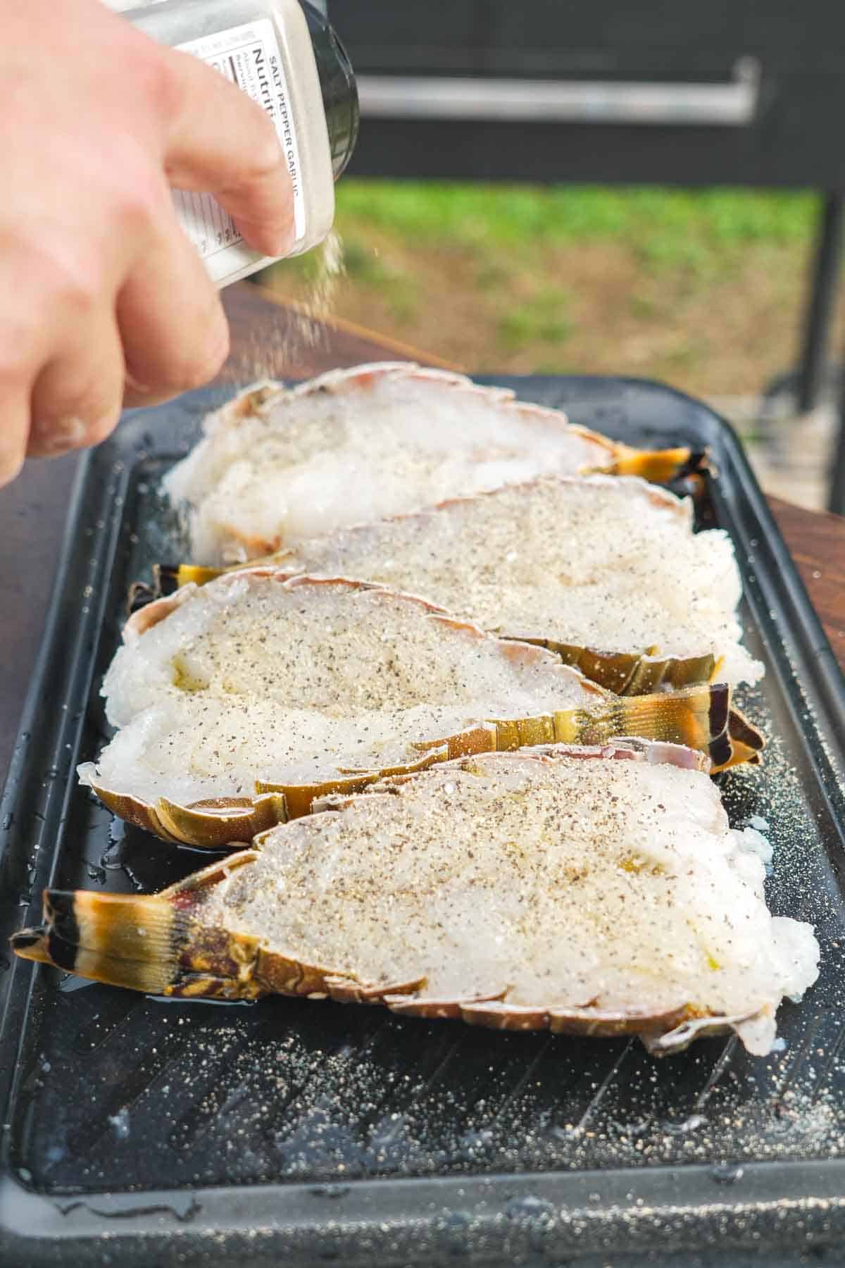 Seasoning raw lobster tails with salt, pepper and garlic powder