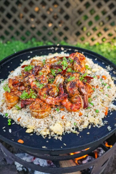 A pile of shrimp fried rice with peas and carrots, eggs, scallion whites and garlic on an open fire skillet on the grill