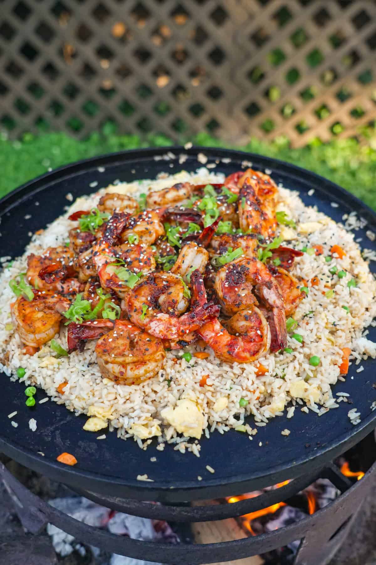 A pile of shrimp fried rice with peas and carrots, eggs, scallion whites and garlic on an open fire skillet on the grill