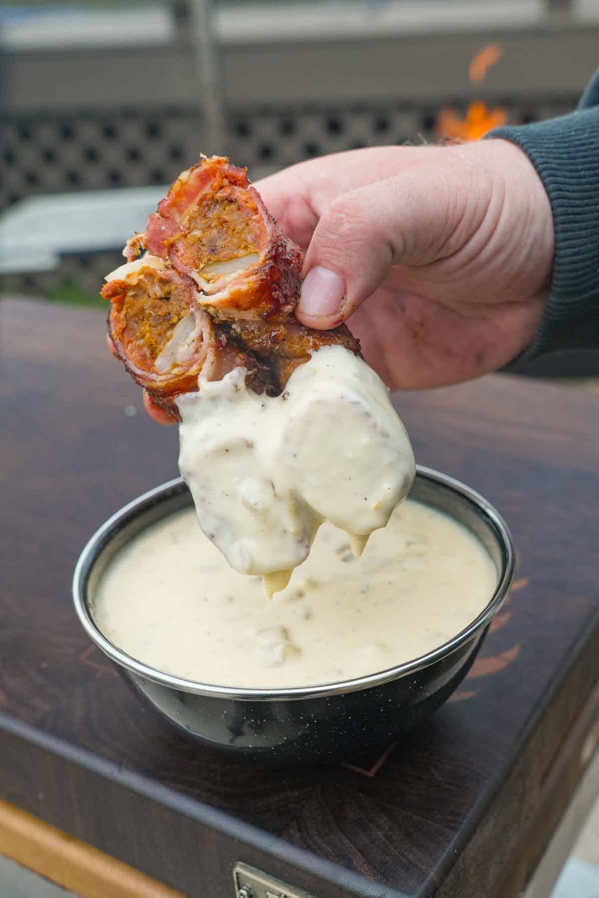 A chorizo stuffed onion ring sliced in half and dipped in a bowl of homemade queso