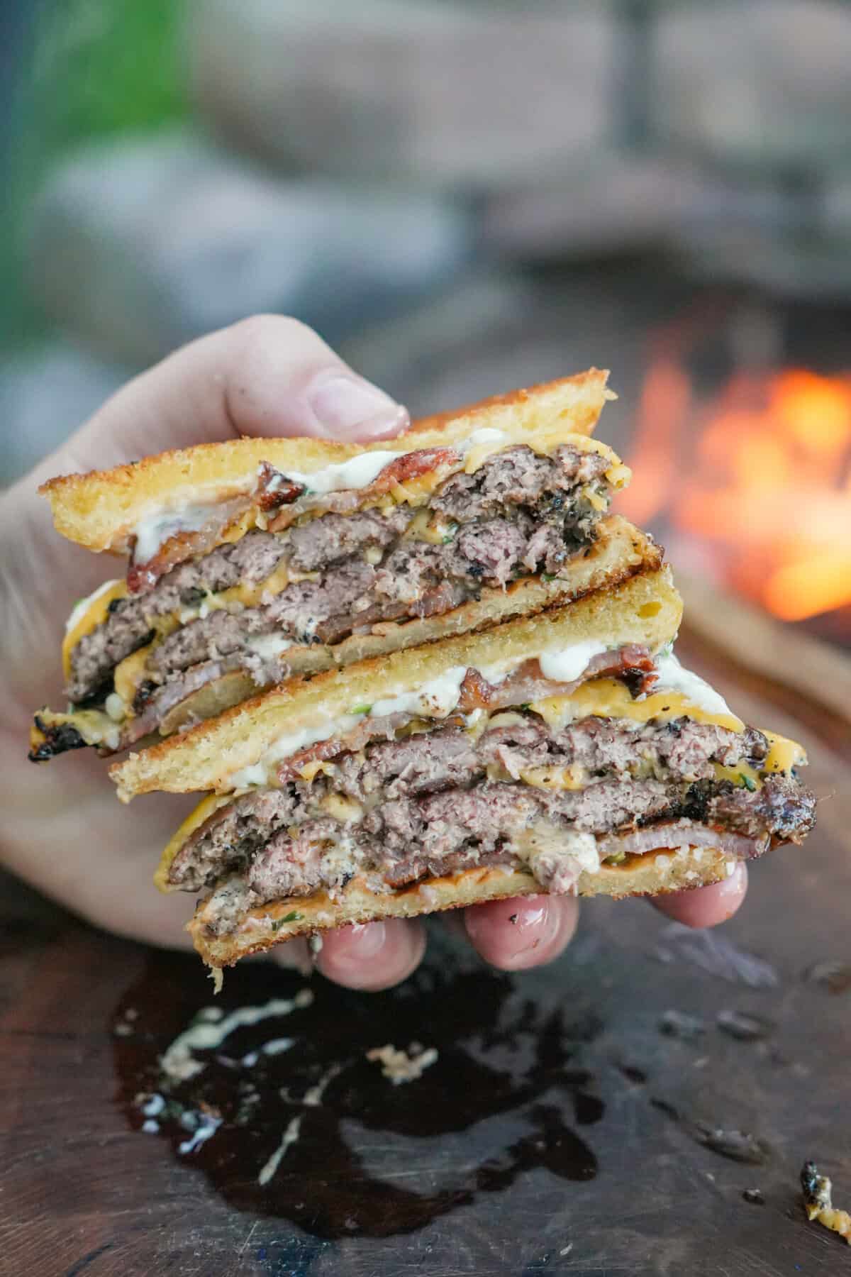 The Garlic Butter Burger is sliced in half showing off all the juicy layers of beef, bacon, cheese, aioli, and bread.