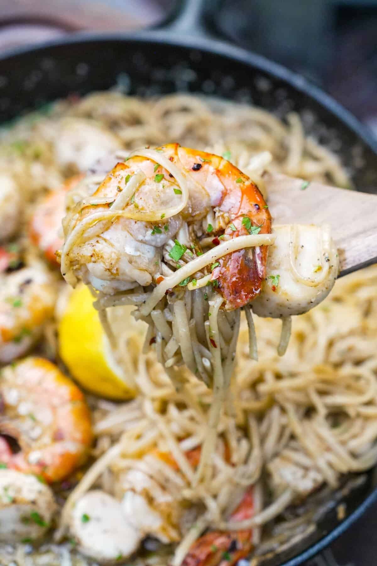 A forkful of seafood scampi with pasta and shrimp and the rest of the dish in the background in a cast iron skillet