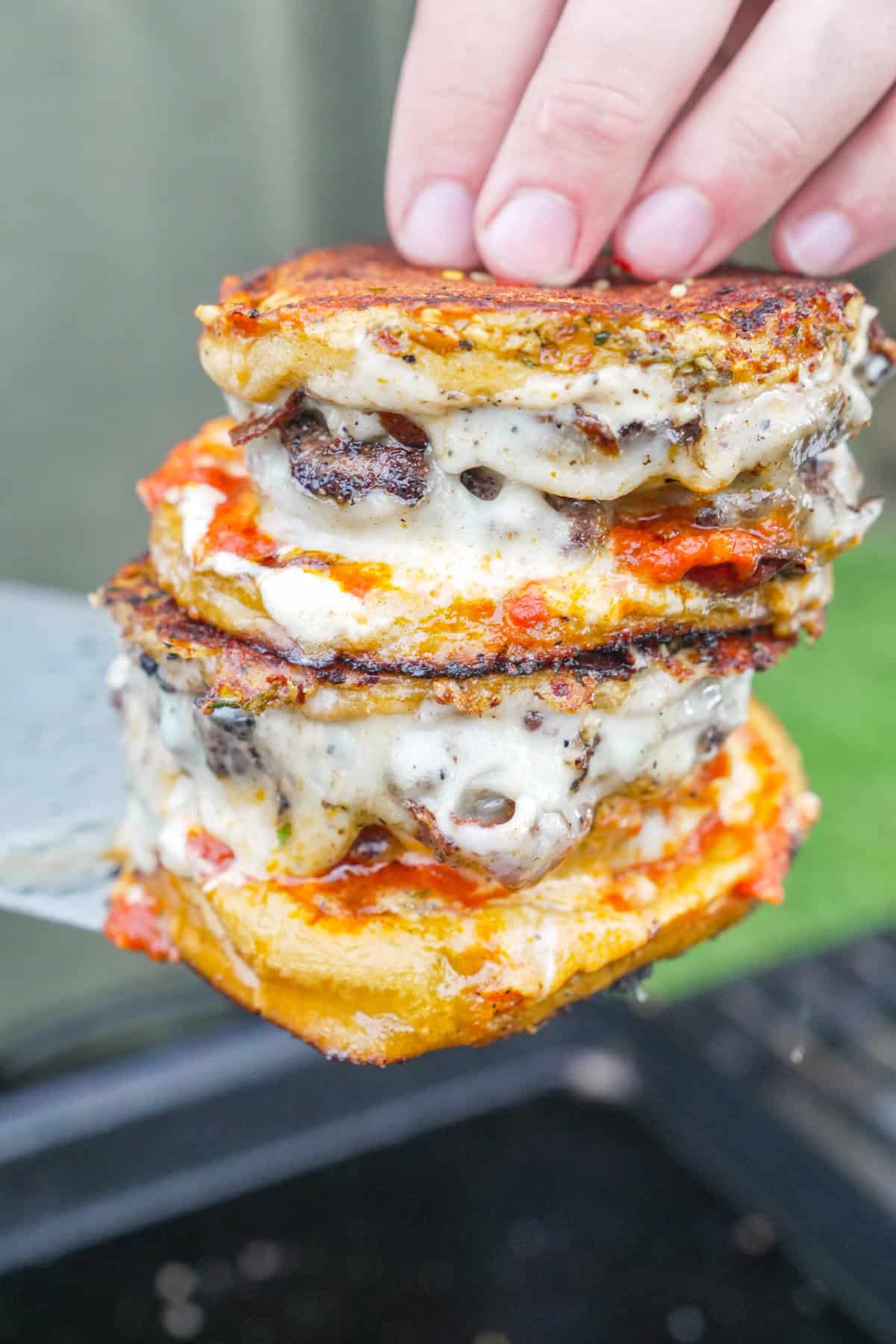 A stack of two pizza smashburgers with mozzarella cheese, beef patties, pizza sauce, garlic aioli and garlic Parmesan butter