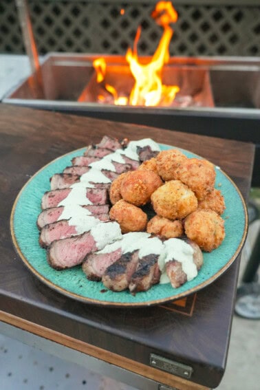 A platter of grilled New York strip steak with jalapeño popper croquettes and avocado ranch dressing in between them