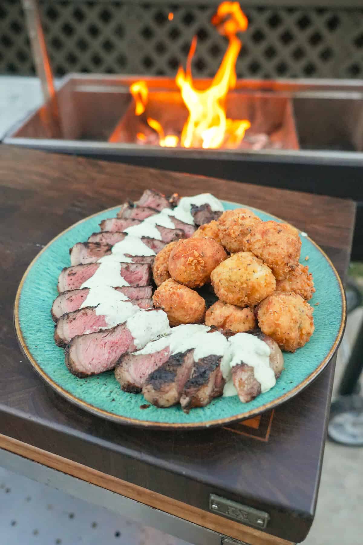A platter of grilled New York strip steak with jalapeño popper croquettes and avocado ranch dressing in between them