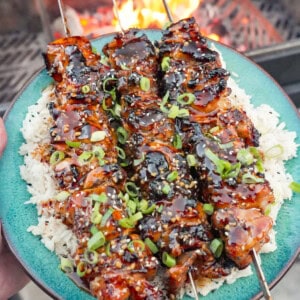 A plate of teriyaki chicken skewers garnished with scallions and sesame seeds over a plate of white rice