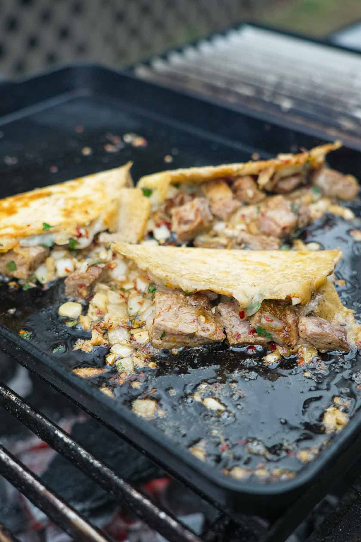 Three Spanish garlic tacos sizzling on a griddle, with pork and cheese and garlic oil