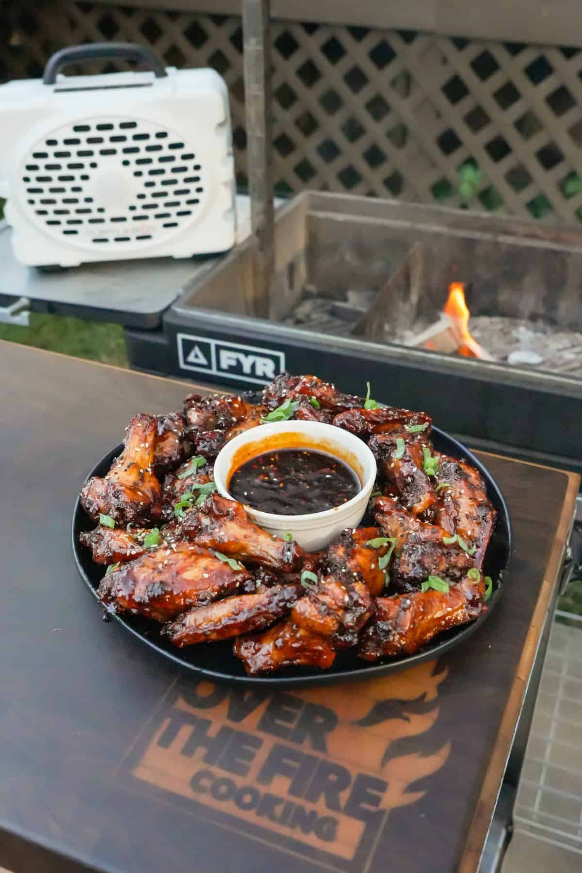 Honey Korean gochujang wings on a plate with sauce in a bowl in the middle and a Turtlebox speaker in the background