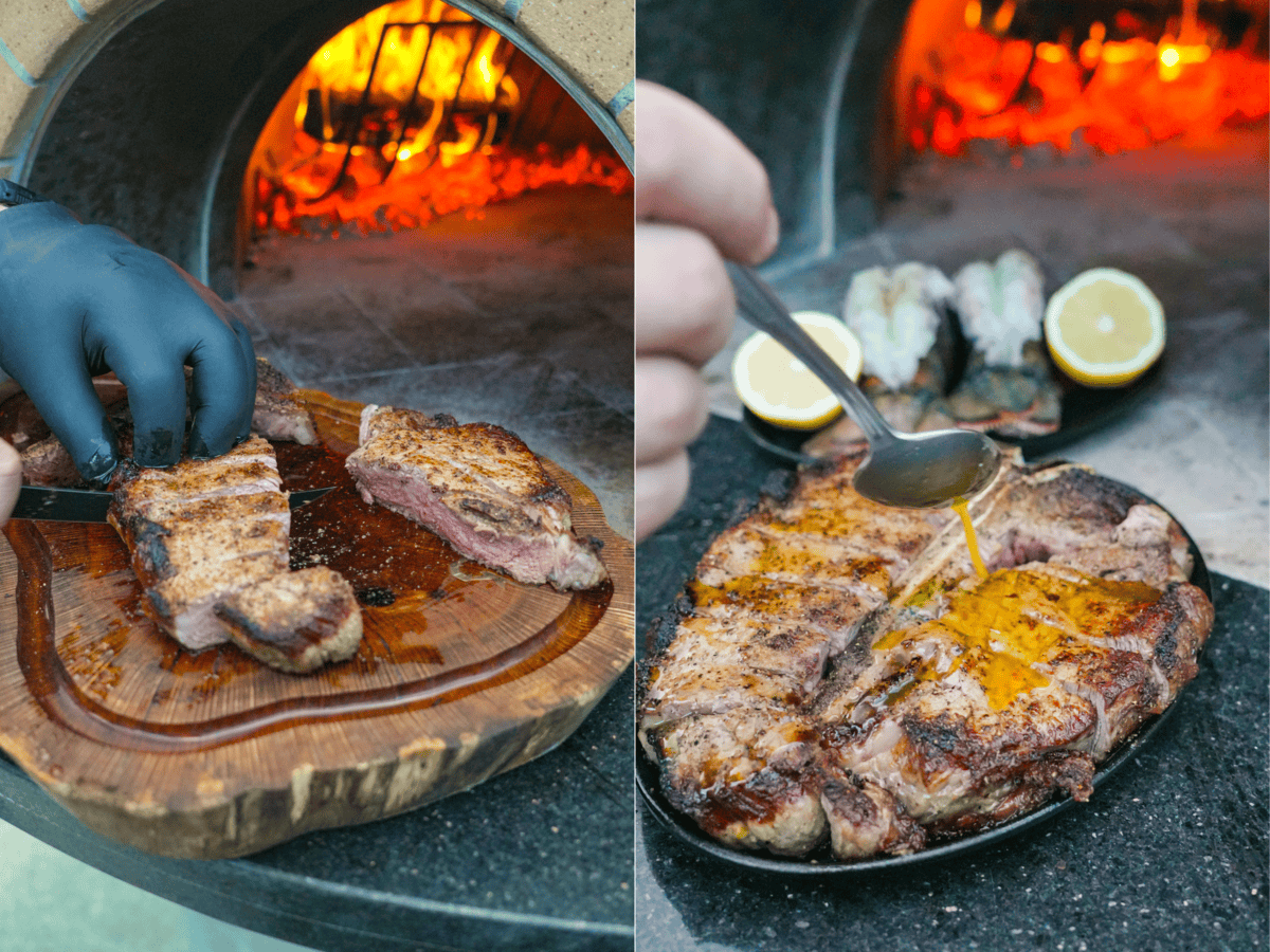 Derek Wolf slicing steak and pouring melted butter over surf and turf platter with lemon garnish by the fire.